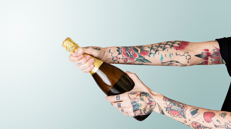 a tattooed hand holding a bottle of champagne