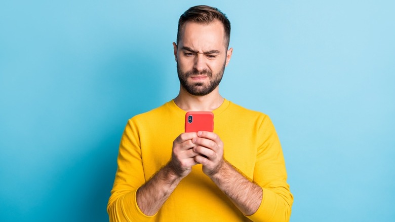 A man cringes while looking at phone