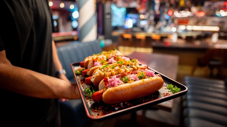 A male server holding a tray of hot dog buns inside a restaurant