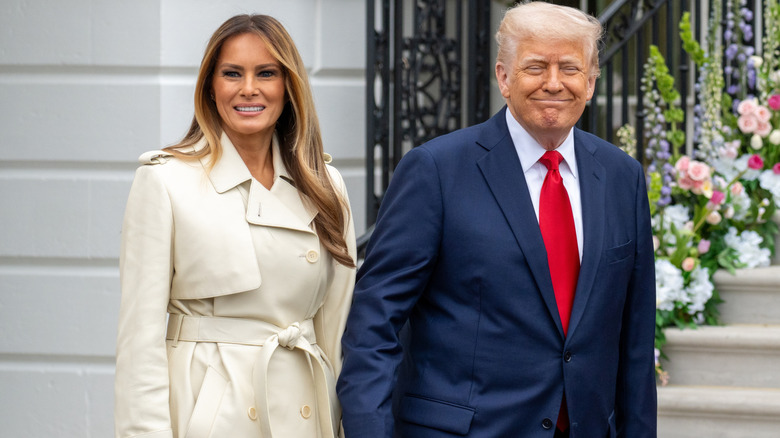 President Donald Trump and first Lady Melania walking in front of a flowery staircase