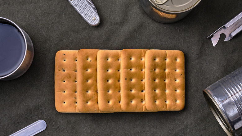 hardtack biscuits on cloth surrounded by canned food and can openers