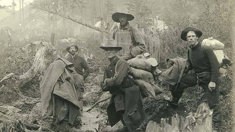 Sepia-toned photo from 1936 of Klondike gold miners carrying supplies on trail in forest