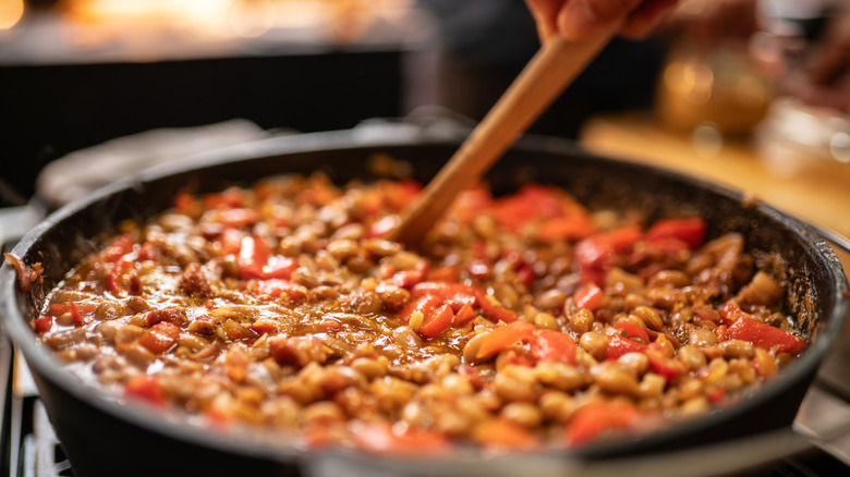 hand stirs wooden spoon in cast iron kettle of baked beans
