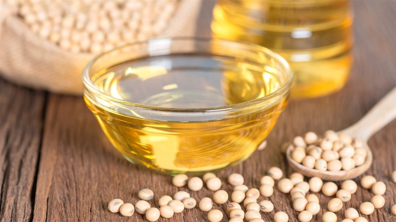 A bowl of soybean oil and some soybeans on a wooden table.