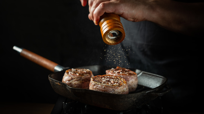 pepper grinding onto steak in pan
