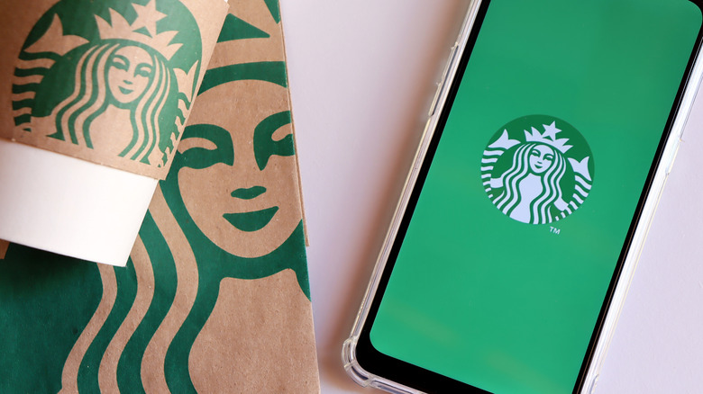 Starbucks shopping bag, Starbucks hot cup, and phone loading Starbucks app
