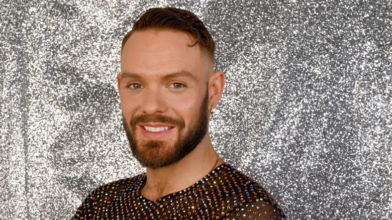 John Whaite smiling for the camera in front of a glittery backdrop