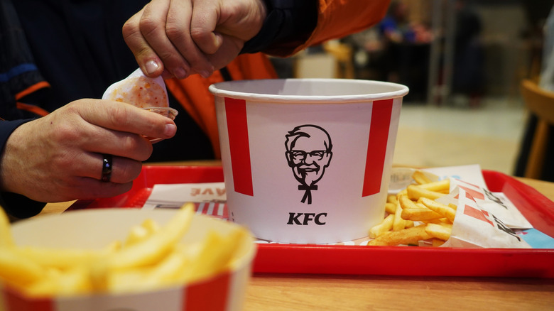 KFC food on tray and hands opening a pot of sauce