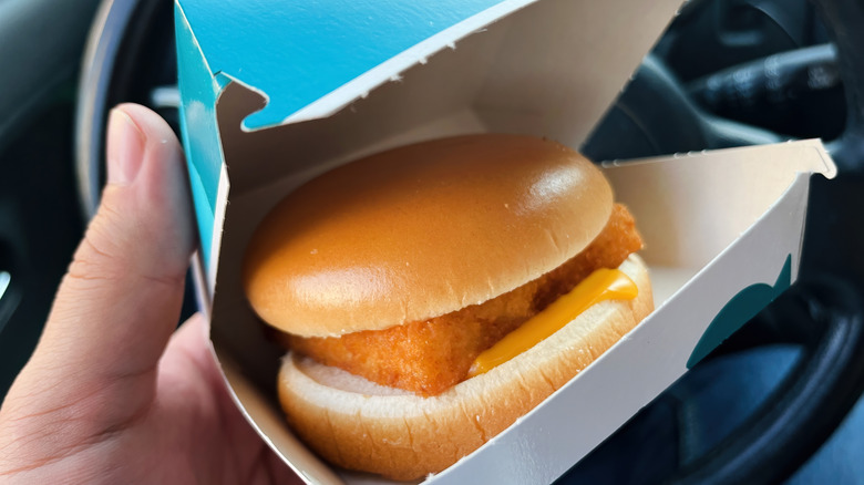 Hand holding a McDonald's Filet-O-Fish sandwich in the box in a car