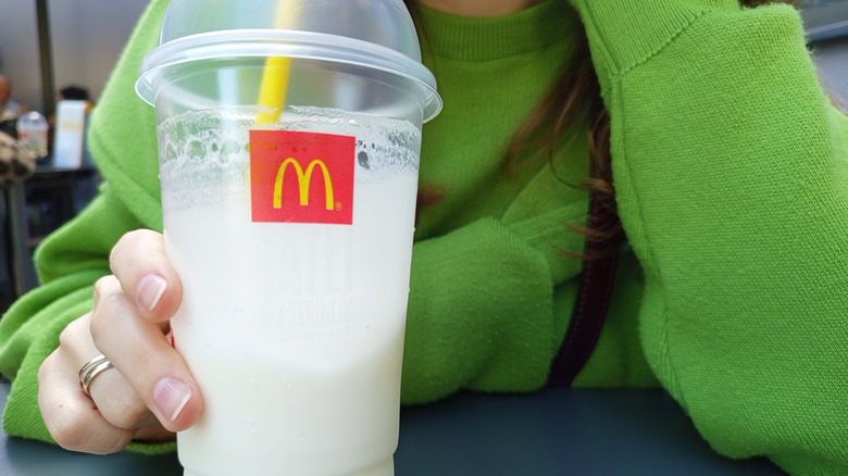 Person in green sweater holding a large McDonald's vanilla milkshake