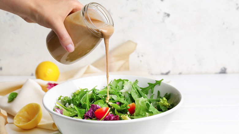 Creamy dressing being poured onto a bowl of salad