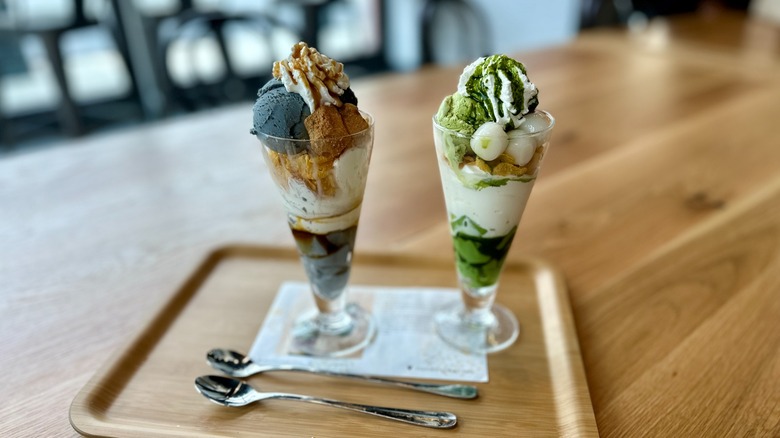 Two ice cream parfaits with spoons on wooden tray inside restaurant.
