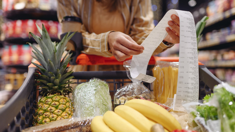 Person looking at receipt with cart of groceries