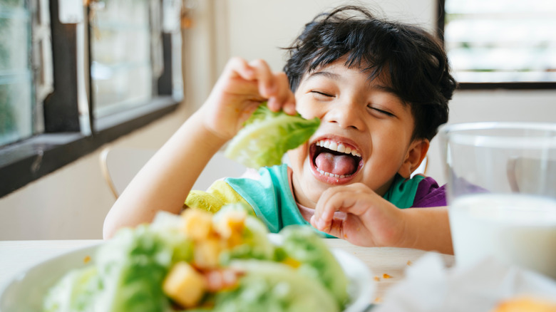 A boy laughing and eating salad 