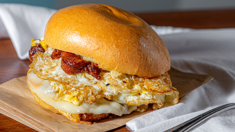 A bacon, egg, and cheese breakfast sandwich on top of brown tissue paper and a white table napkin