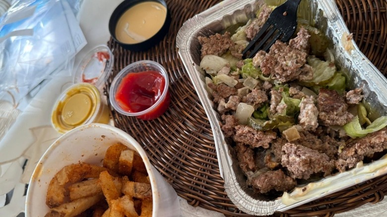 A Five Guys burger bowl, Cajun fries in a cup, and open condiment containers of ketchup and mustard