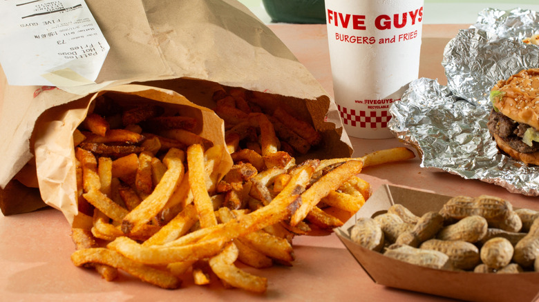Five Guys Cajun fries spilling out of a brown paperbag. Also visible are a burger, soda cup, and peanuts