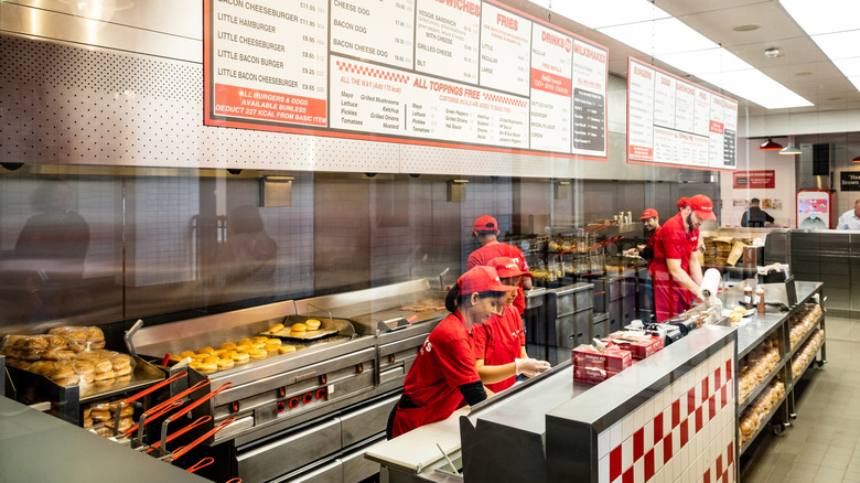 Uniformed employees stand behind the counter inside a Five Guys Restaurant, the menu board above them visible