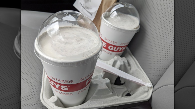 Two Five Guys milkshakes in a takeout container placed in the front seat of a car