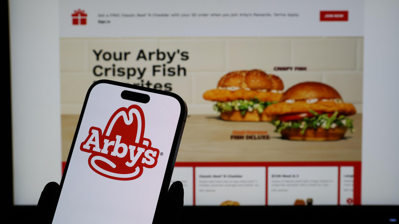 Arby's mobile app on phone in front of Arby's drive-thru screen