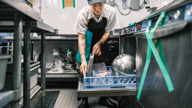 Dishwasher in restaurant kitchen bending over machine