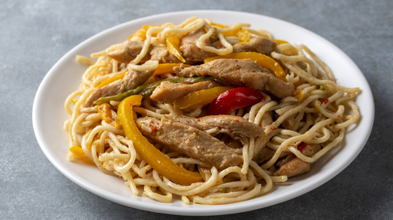 A plate of chicken and noodles with bell peppers