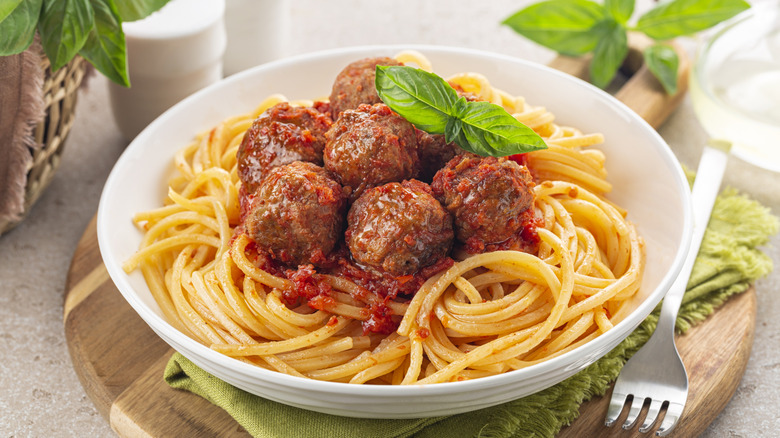 A bowl of spaghetti and meatballs garnished with fresh basil on a nicely set table