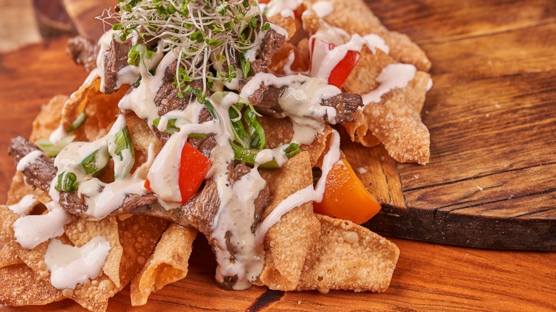 Pile of nachos with beef, sprouts, and cream on wood table