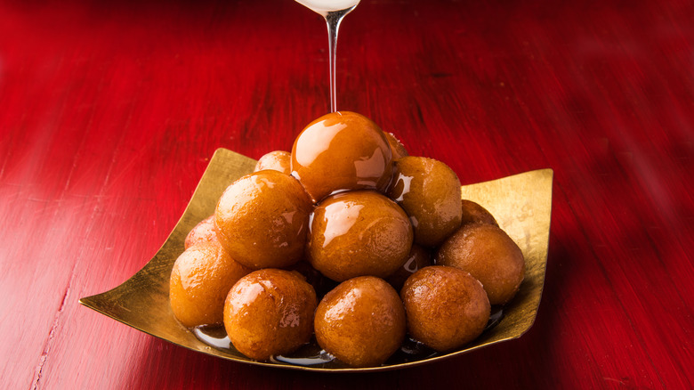 Gold plate of gulab jamun with syrup being poured over