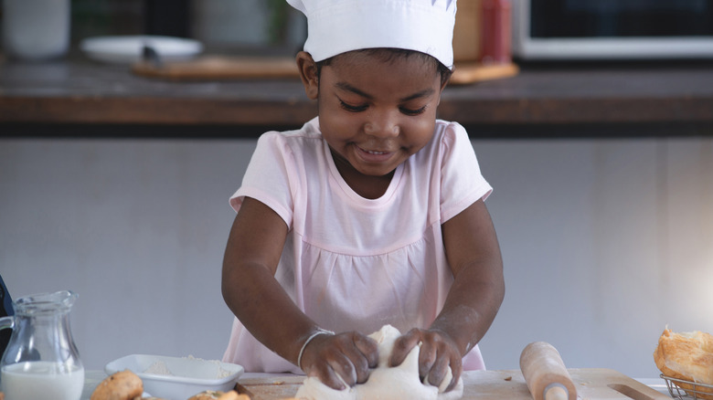 Young girl in a chef hat rolling out dough