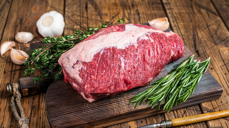 Raw brisket on wooden board with herbs