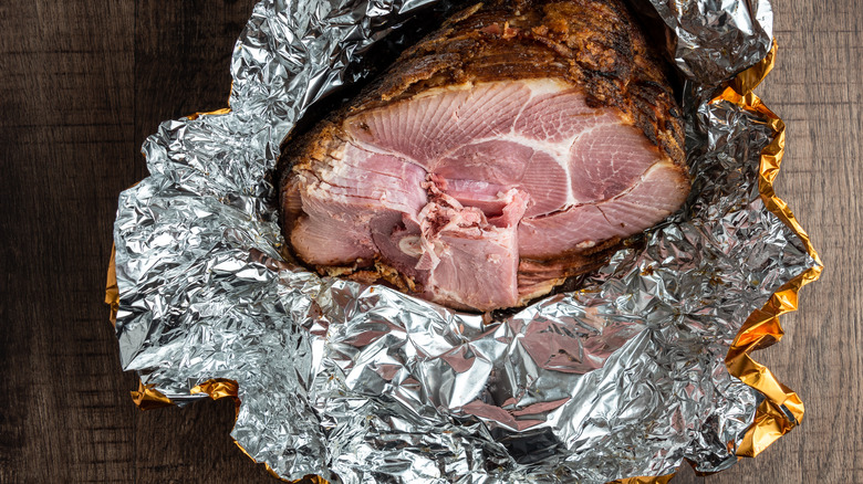 Honey baked ham in foil wrapping on a wood background