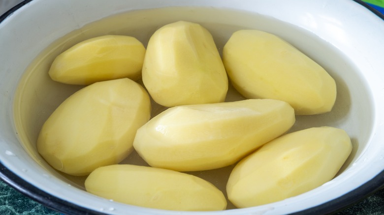 Peeled potatoes in bowl of water