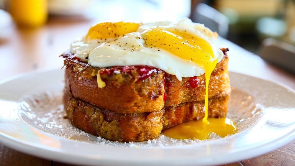 Stack of French toast topped with two runny, fried eggs.