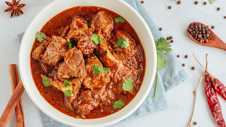 White bowl full of meat and red sauce next to spices