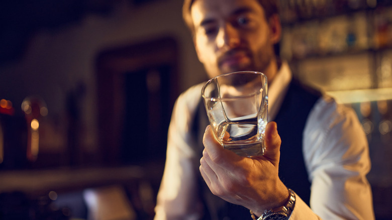 Bartender holding up an empty whiskey glass and looking thoughtful
