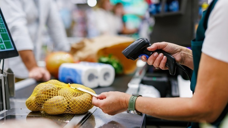 Person scanning barcode on bag of potatoes at checkout counter.