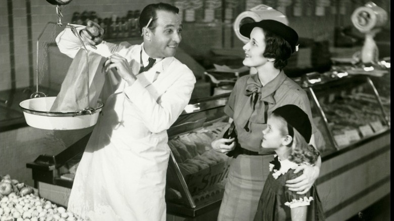 Man weighs produce at a grocery store with woman and child.