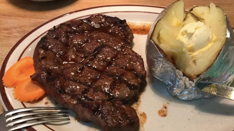A plate with a steak, baked potato, and carrots.