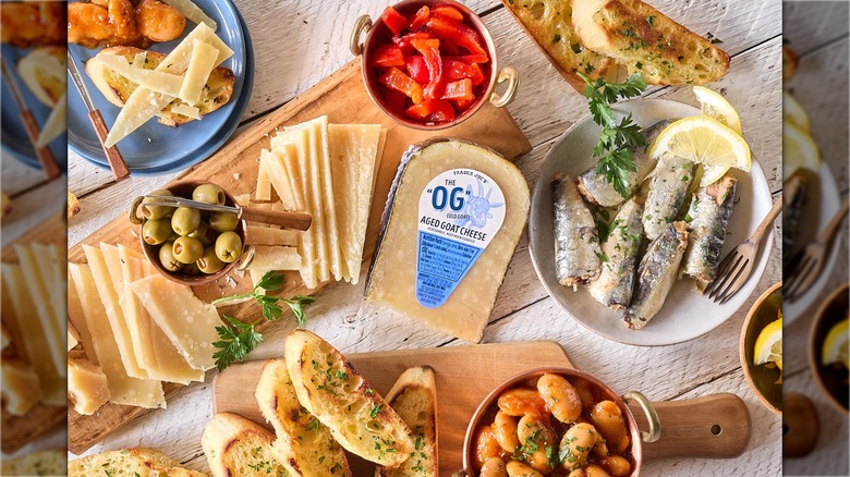 Pack of aged goat cheese in the center of a charcuterie spread with toast, cheese, fish, and garnishes.