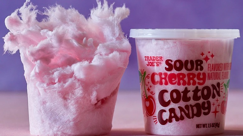 A container of sour cherry flavored cotton candy next to the cotton candy itself.