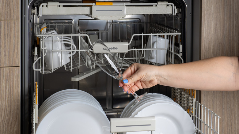 Person holding a glass in front of a dishwasher open and loaded with clean dishes
