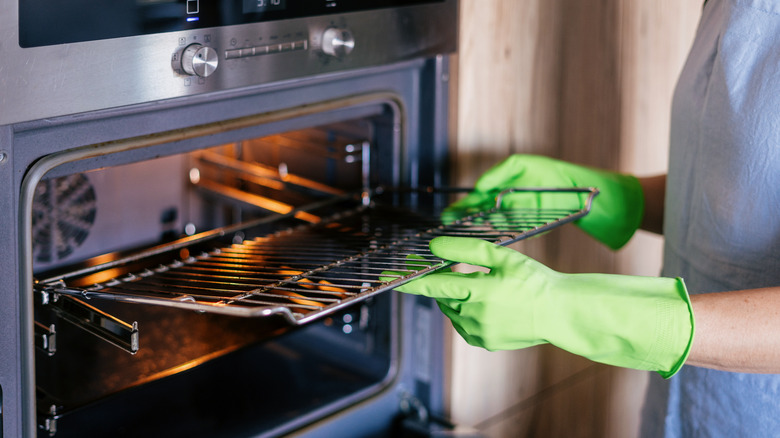 A person wearing gloves removes a rack from an open oven.