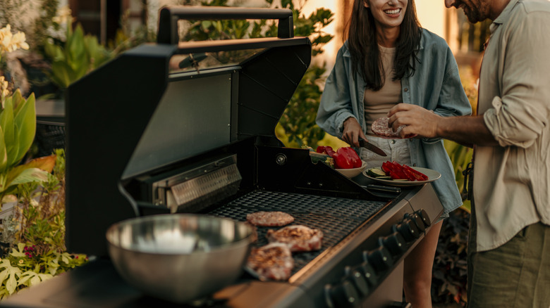 Smiling man and woman at an outdoor grill where food is cooking