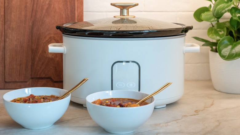 Slow cooker with two bowls of chili on kitchen counter.