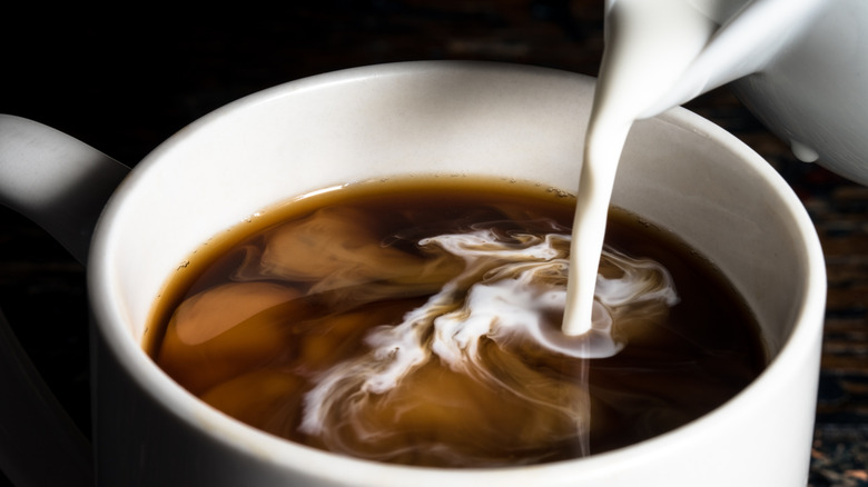 Cream pouring into cup of coffee.