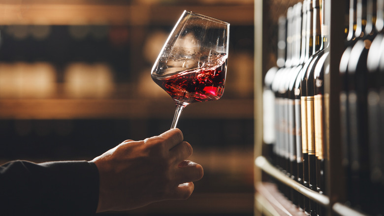 Hand swirling glass of red wine in wine cellar.