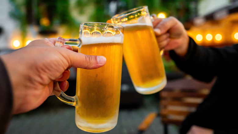 Two hands clinking mugs of light beer.