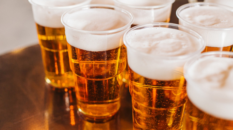 Multiple plastic cups of beer lined up on bar.