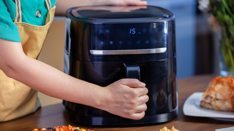 An aproned person's hand is on an air fryer's handle.